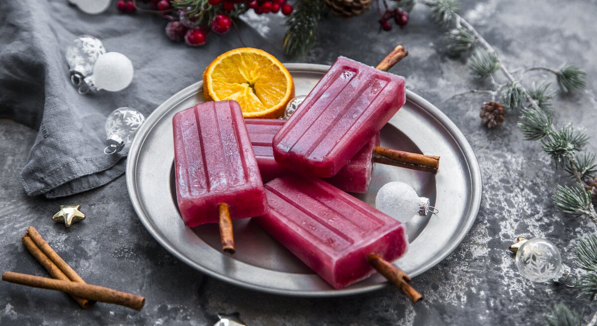 Glühwein-Eis am Stiel angerichtet auf einem silbernem Teller. Drumherum finden sich verschiedene, weihnachtliche Deko-Elemente.