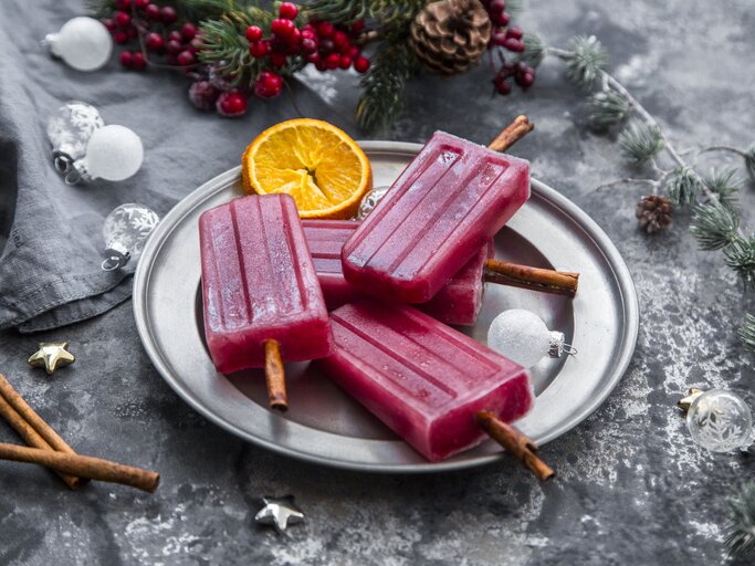 Glühwein-Eis am Stiel angerichtet auf einem silbernem Teller. Drumherum finden sich verschiedene, weihnachtliche Deko-Elemente. | © Getty Images/Westend61