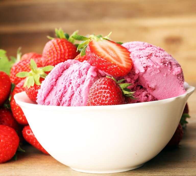 Frontal: eine weiße Porzellanschale mit zwei Kugeln Milchmädchen-Eis mit Erdbeeren auf einem Untergrund aus Holz. | © Shutterstock / beats1