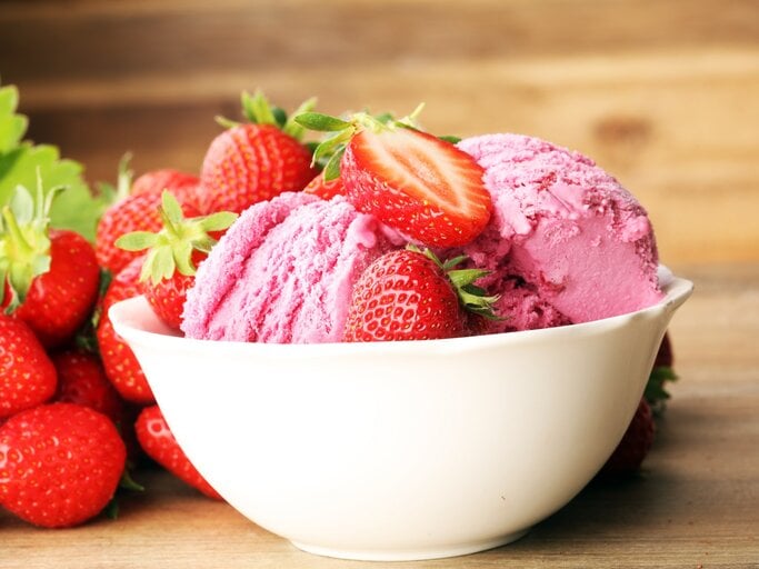 Frontal: eine weiße Porzellanschale mit zwei Kugeln Milchmädchen-Eis mit Erdbeeren auf einem Untergrund aus Holz. | © Shutterstock / beats1