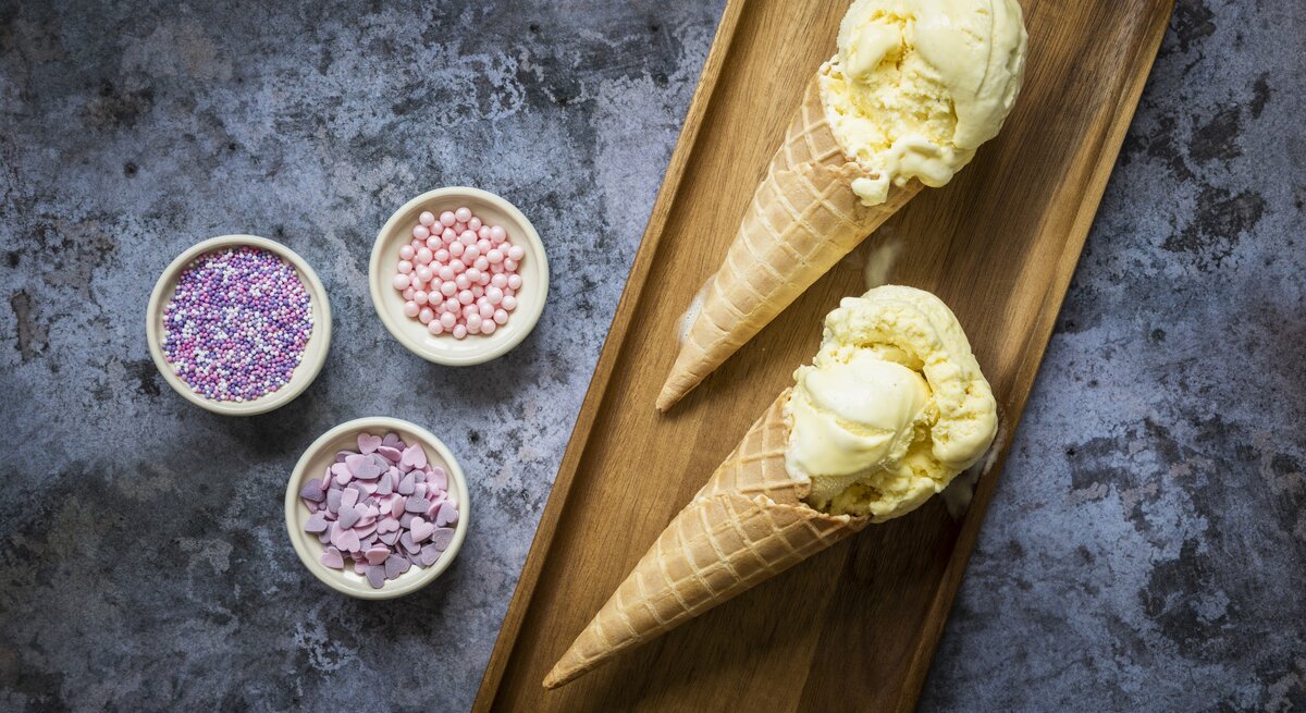 Eiscreme in Waffeln auf einem kleinen Holzbrett mit bunten Zuckerperlen auf einem dunklen Steintisch.