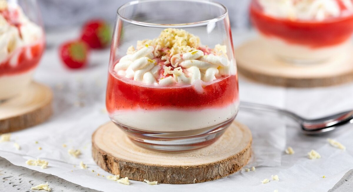 In einem Glas ist ein Spaghetti-Eis mit Mascarpone und Erdbeersauce angerichtet. Es ist mit weißer Schokolade bestreut. 