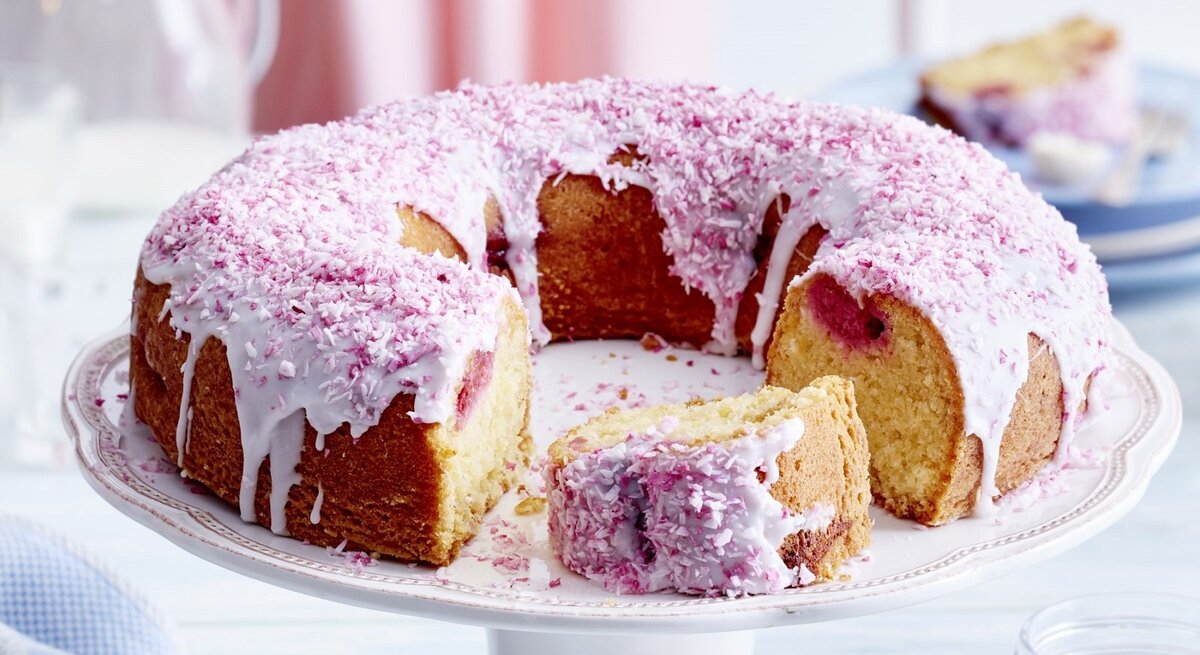 Auf einem Teller liegt ein Kokos-Himbeer-Kuchen. Er ist mit rosa Creme und Haferflocken dekoriert. 