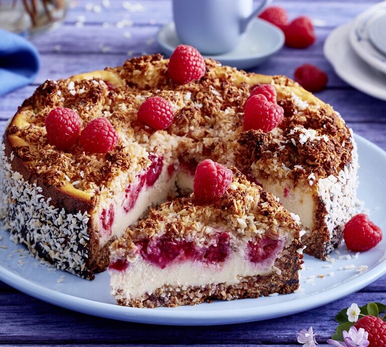 Auf einem Teller liegt ein Schmandkuchen mit Himbeeren. Er ist mit Himbeeren und Kokosraspeln dekoriert. | © EAT CLUB / Isabell Triemer 