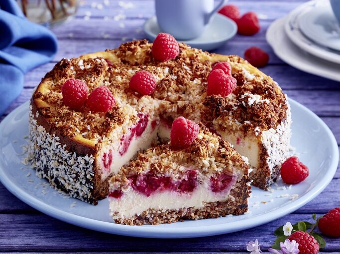 Auf einem Teller liegt ein Schmandkuchen mit Himbeeren. Er ist mit Himbeeren und Kokosraspeln dekoriert. | © EAT CLUB / Isabell Triemer 