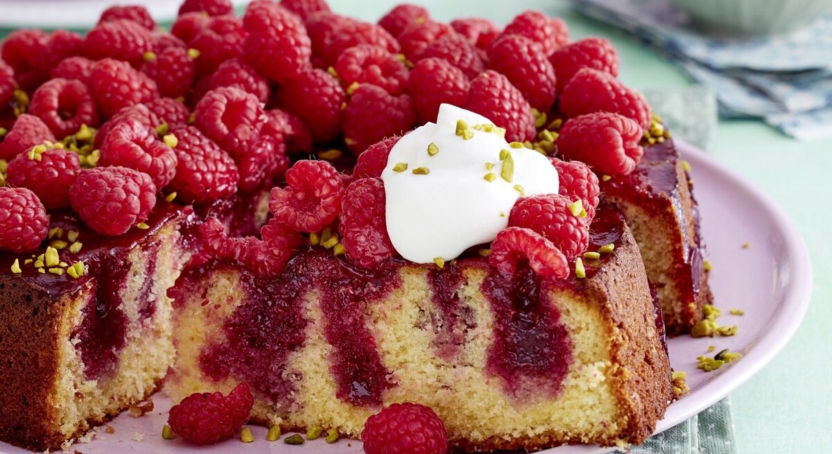 Auf einem pinken Teller liegt ein Himbeer-Zitrus-Kuchen. Er ist mit einem Klecks Schlagsahne bedeckt.
