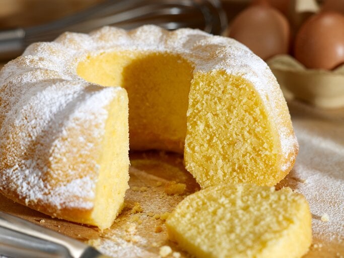 Heller Gugelhupf mit Puderzucker, daneben ein Schneebesen und mehrere Eier.  | © AdobeStock/Florian Biber