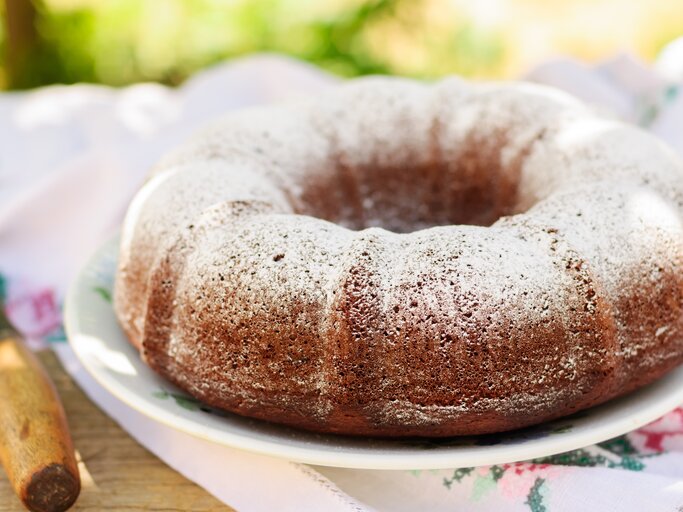 Gugelhup mit Puderzucker bestäubt auf weißem Teller in sommerlichem Ambiente. | © Shutterstock/Tatiana Vorona