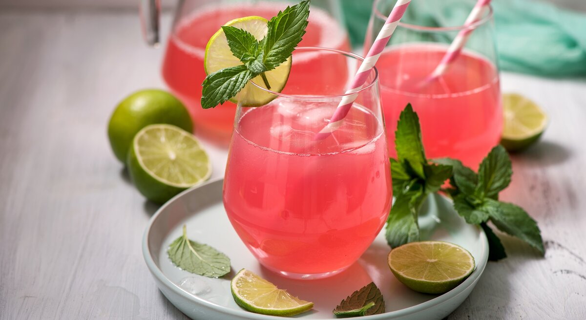 Zwei Gläser Rhabarber-Holunder-Spritz mit Strohhalmen, Minze und Limettenscheiben.