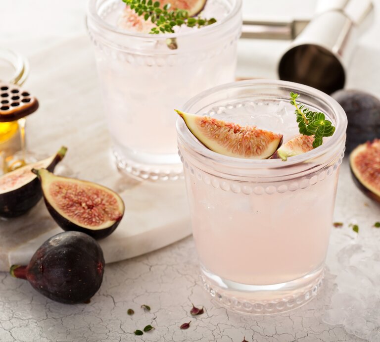 Zwei Gläser Feigen-Spritz mit frischen Feigen und Kräutern, drumherum Bar-Zubehör und Zutaten. | © Adobe Stock/ fahrwasser
