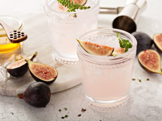 Zwei Gläser Feigen-Spritz mit frischen Feigen und Kräutern, drumherum Bar-Zubehör und Zutaten. | © Adobe Stock/ fahrwasser