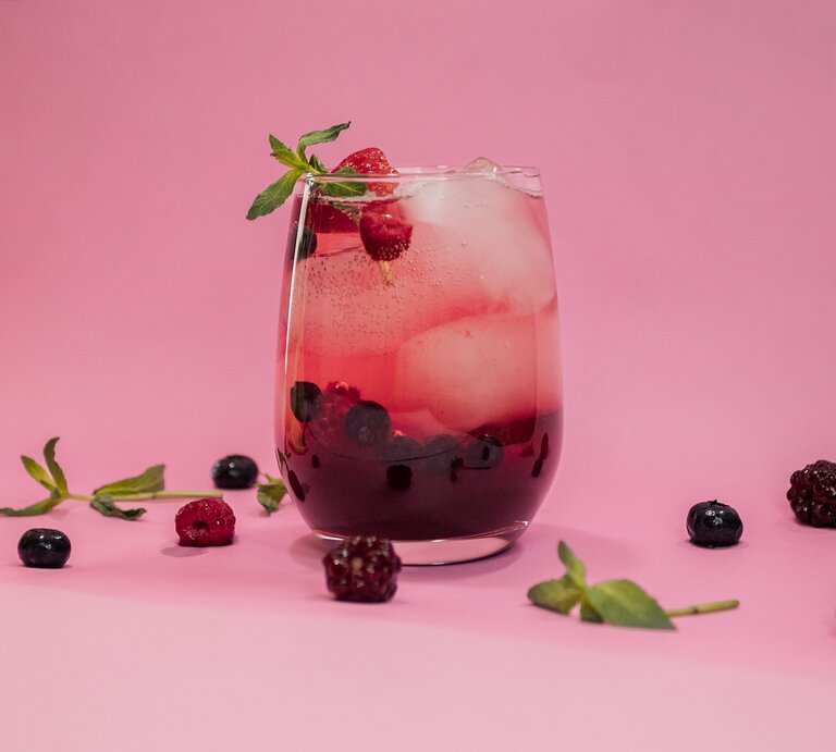 Ein Glas mit Lillet Spritz, Eiswürfeln, Beeren und Minze vor rosa Hintergrund, drumherum liegen Beeren und Minze. | © Adobe Stock/ francisco