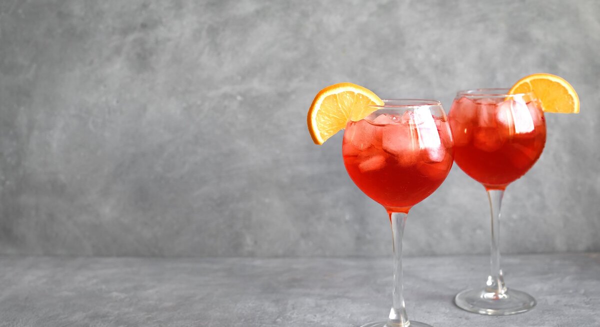Zwei Gläser mit Negroni Spritz vor einem grauen Hintergrund.
