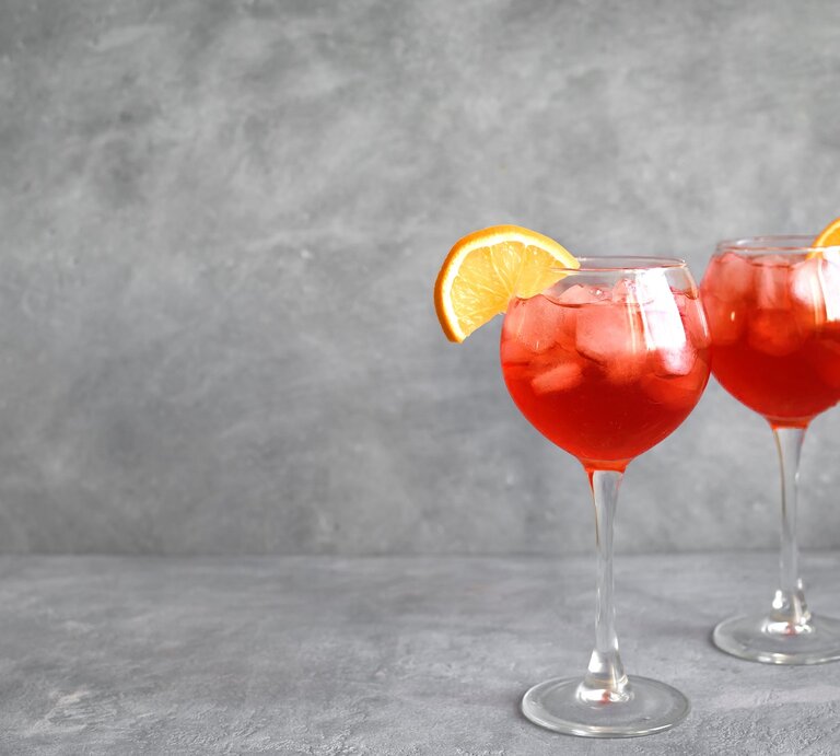 Zwei Gläser mit Negroni Spritz vor einem grauen Hintergrund. | © Shutterstock/Oksana Mizina