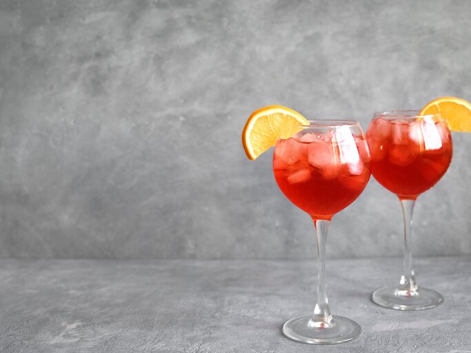 Zwei Gläser mit Negroni Spritz vor einem grauen Hintergrund. | © Shutterstock/Oksana Mizina