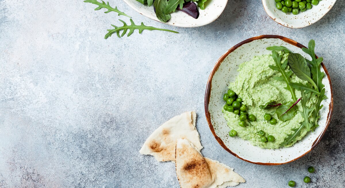 Erbsen-Guacamole garniert mit Rucola in Schüssel vor blauem Untergrund