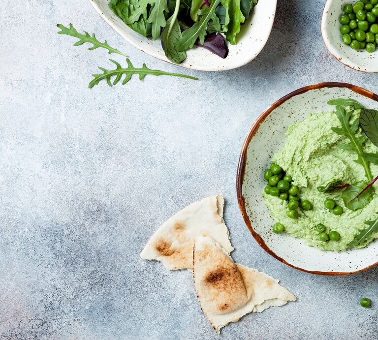 Erbsen-Guacamole garniert mit Rucola in Schüssel vor blauem Untergrund | © Getty Images/ sveta_zarzamora