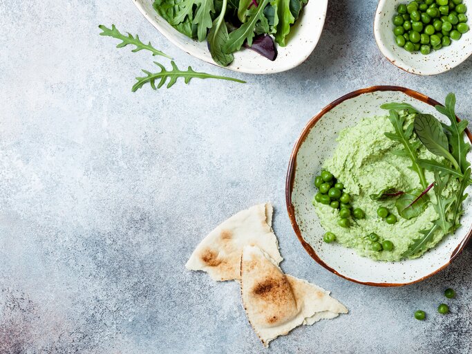 Erbsen-Guacamole garniert mit Rucola in Schüssel vor blauem Untergrund | © Getty Images/ sveta_zarzamora