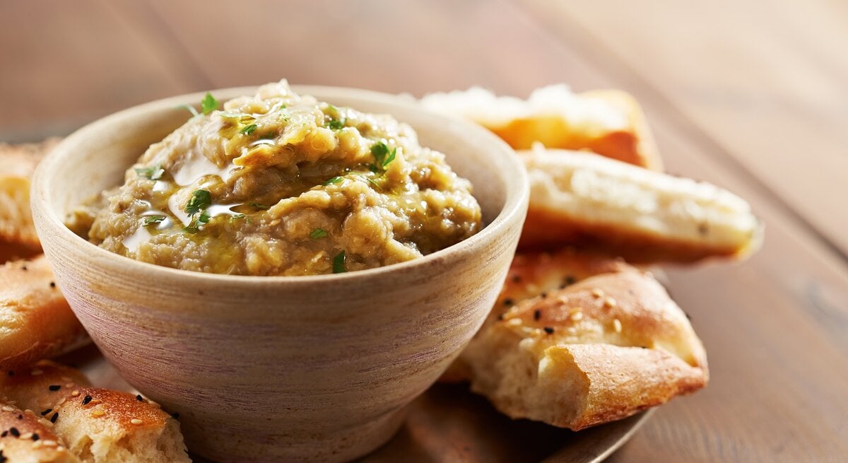 Eine Schale Lib el Kousa, ein levantinischer Zucchini-Knoblauch-Dip, auf einem Tablett, darauf außerdem Fladenbrot-Stücke.