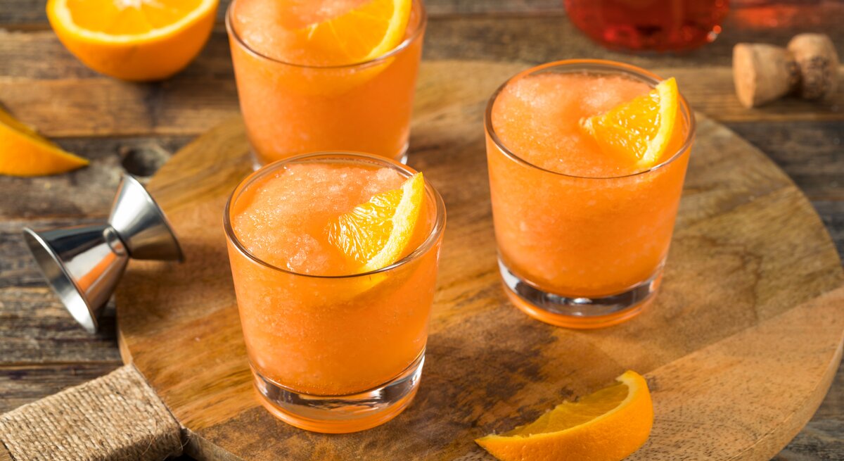 Drei Gläser Frozen Aperol Spritz auf Holzbrett. 