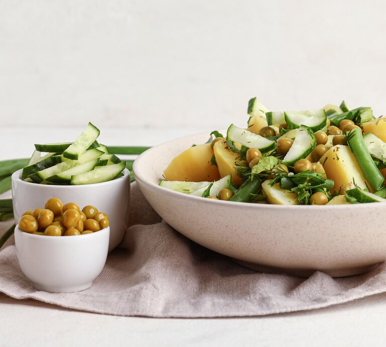 Eine weiße Schale mit dem Kartoffelsalat. Daneben drei kleine Schalen mit den weiteren Zutaten. Alles auf hellem Unter- und Hintergrund. | © Shutterstock/ Pixel-Shot