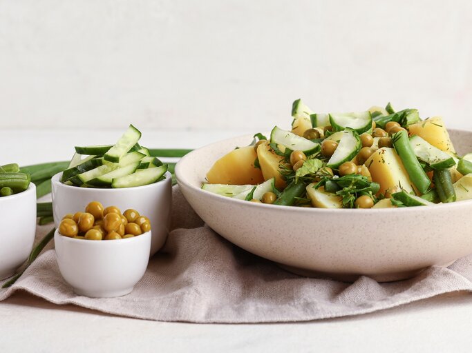Eine weiße Schale mit dem Kartoffelsalat. Daneben drei kleine Schalen mit den weiteren Zutaten. Alles auf hellem Unter- und Hintergrund. | © Shutterstock/ Pixel-Shot