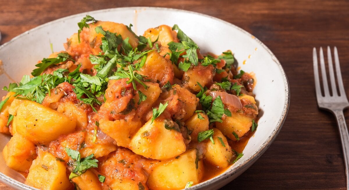 Kartoffelsalat mit Harissa-Dressing und Petersilie in einer Schüssel, daneben eine Gabel.