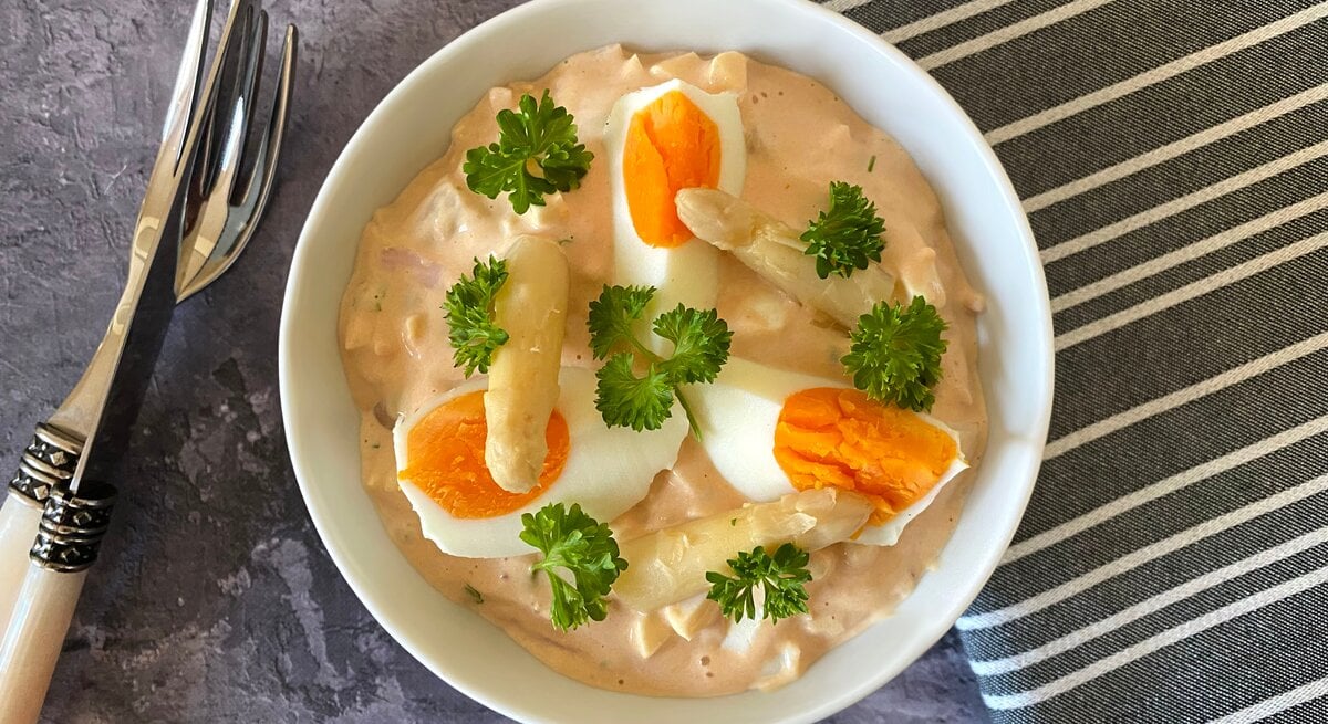 Weiße Schale gefüllt mit Eiersalat mit Spargel auf dunklem Untergrund. 