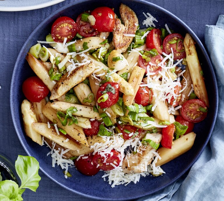 Italienischer Spargel-Mix mit Parmesan in dunkler Schüssel auf dunkelblauem Untergrund. Daneben Küchentuch, Besteck und Basilikumpflanze.  | © EAT CLUB / Isabell Triemer