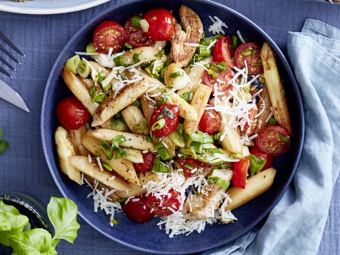 Italienischer Spargel-Mix mit Parmesan in dunkler Schüssel auf dunkelblauem Untergrund. Daneben Küchentuch, Besteck und Basilikumpflanze.  | © EAT CLUB / Isabell Triemer