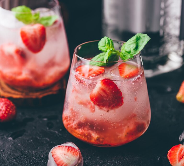 Erdbeer-Gin-Tonic auf einem dunklen Untergrund. Daneben liegen verschiedene Zutaten. | © Getty Images / Seva_blsv