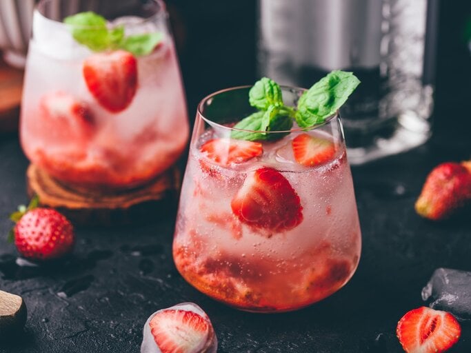 Erdbeer-Gin-Tonic auf einem dunklen Untergrund. Daneben liegen verschiedene Zutaten. | © Getty Images / Seva_blsv