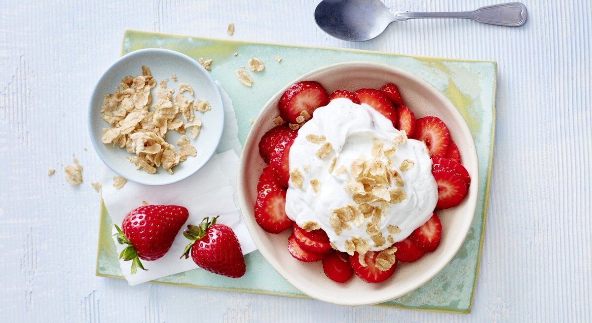 In einer Schüssel sind Erdbeeren mit Vanillequark angerichtet. Darüber sind Dinkel-Flocken gegeben. 