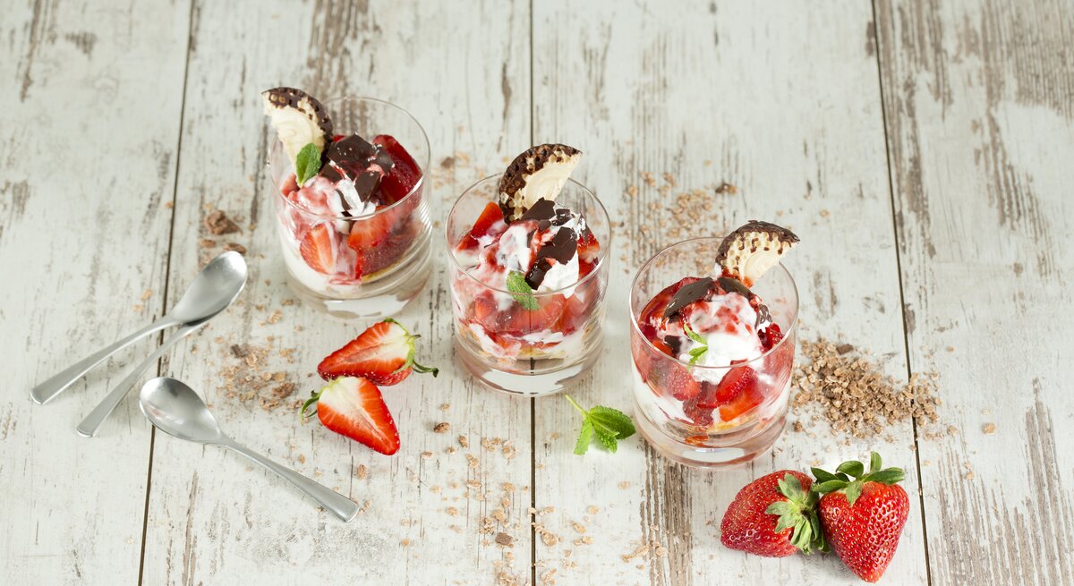 Drei Schalen mit Schokokuss-Erdbeer-Dessert auf weißem Holzuntergrund. 