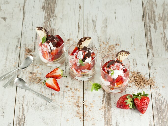 Drei Schalen mit Schokokuss-Erdbeer-Dessert auf weißem Holzuntergrund.  | © Getty Images/Westend61