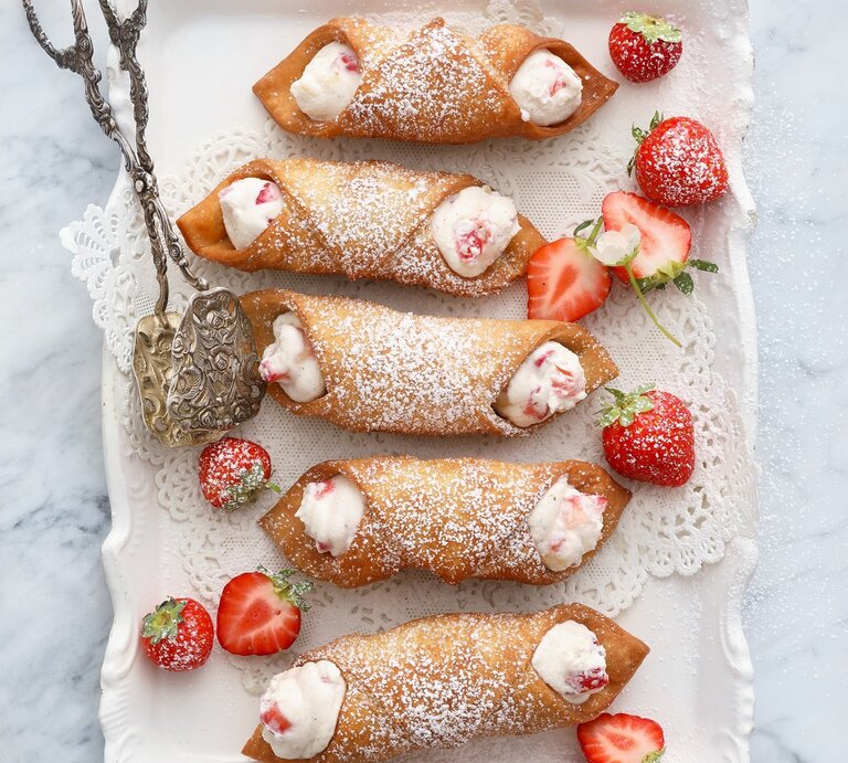 Italienische Cannoli mit Ricota-Erdbeer-Füllung, bestäubt mit Puderzucker und serviert auf einem weißen, verzierten Kuchenteller, angereicht mit frischen Erdbeeren.  | © StockFood / Jalag / Neubauer, Mathias