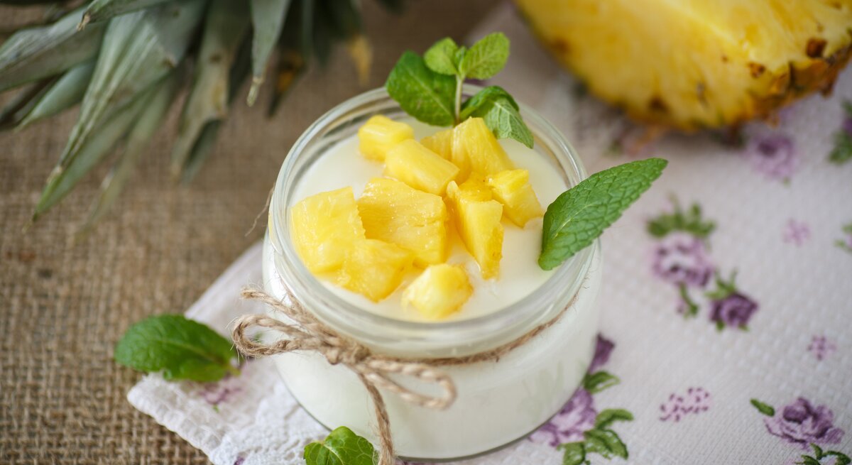 Quark-Dessert mit Ananas im Glas. Angerichtet ist das Ganze auf einem braunen Leinentuch.