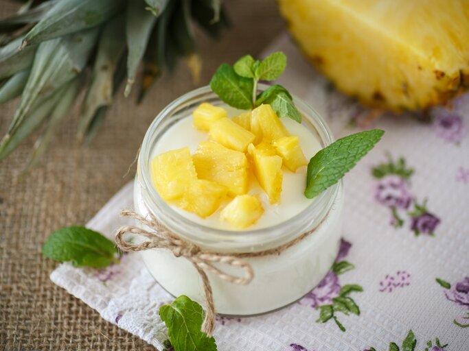 Quark-Dessert mit Ananas im Glas. Angerichtet ist das Ganze auf einem braunen Leinentuch. | © GettyImages/peredniankina