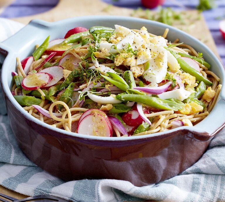 Eine Schüssel Bohnen-Nudel-Salat mit Eiern steht auf einem blau-weißem Tuch. Im Hintergrund sieht man Radieschen. | © EAT CLUB / Isabell Triemer