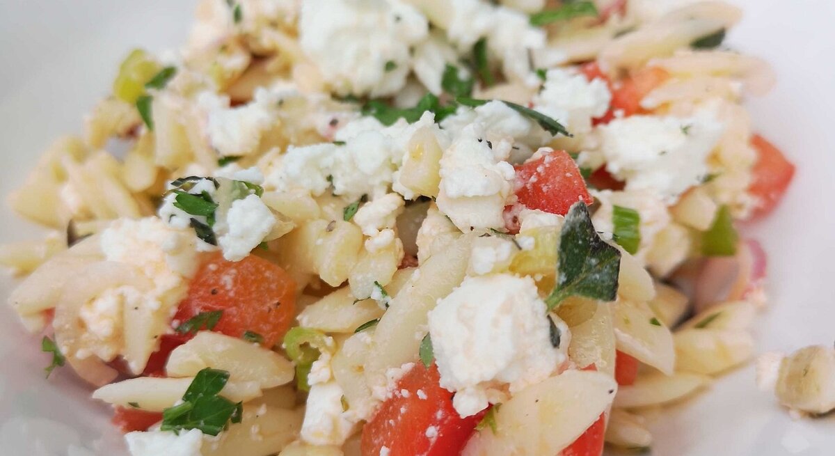 Griechischer Nudelsalat mit Feta, Melone, Tomate und Oliven auf weißem Teller. 