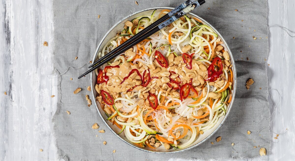 Veganer Glasnudelsalat mit leckerer Erdnusssoße auf einem grauen Tuch. Dazu Stäbchen. 