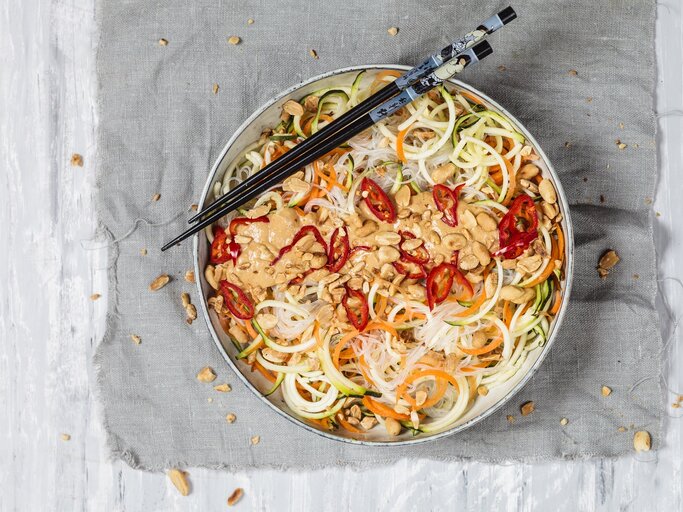 Veganer Glasnudelsalat mit leckerer Erdnusssoße auf einem grauen Tuch. Dazu Stäbchen.  | © Getty Images/ Westend61