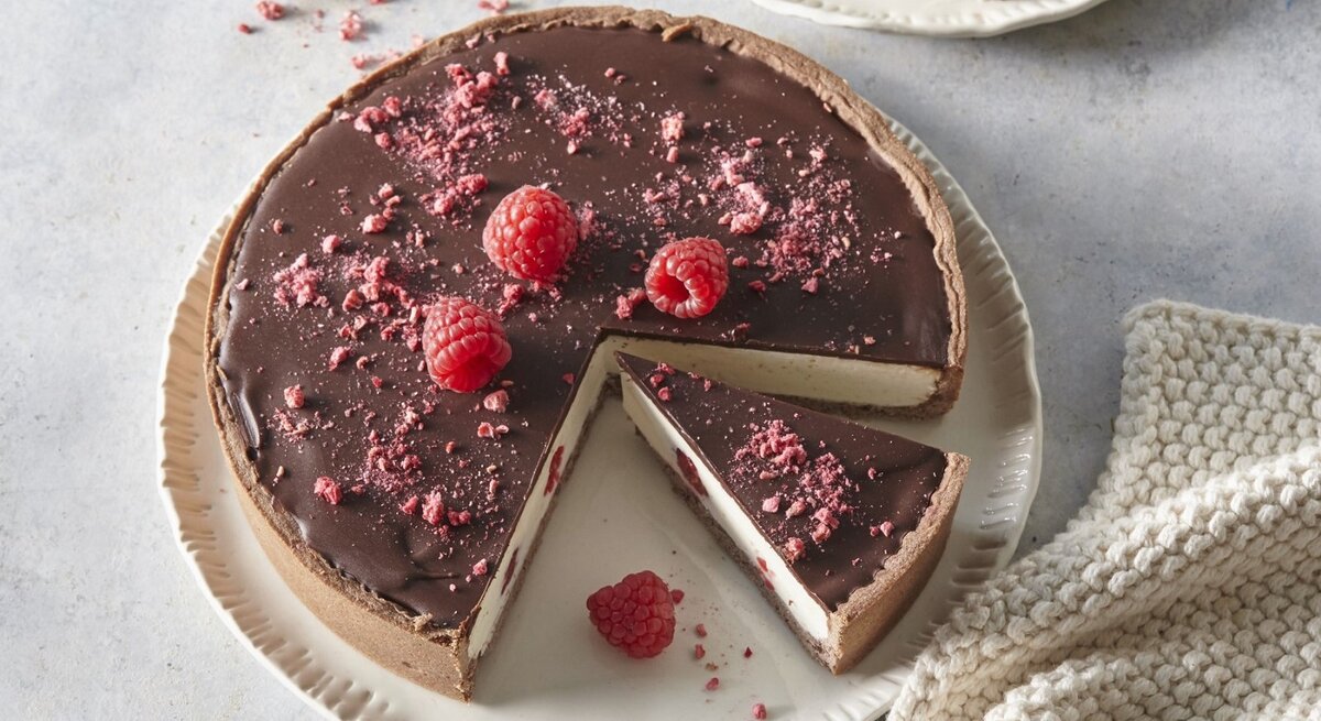Auf einem Teller steht ein Käsekuchen mit Schokolade und Himbeeren. Er ist mit Himbeeren und Schokolade überzogen. 