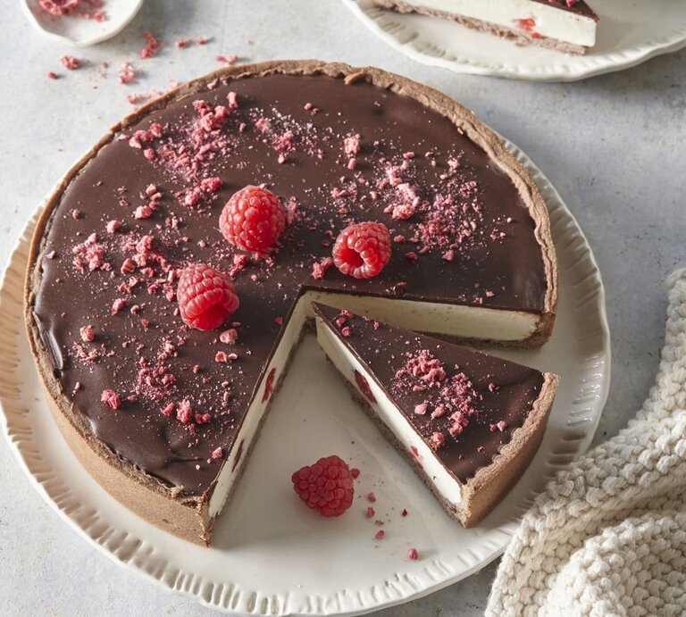 Auf einem Teller steht ein Käsekuchen mit Schokolade und Himbeeren. Er ist mit Himbeeren und Schokolade überzogen.  | © StockFood / Profimedia