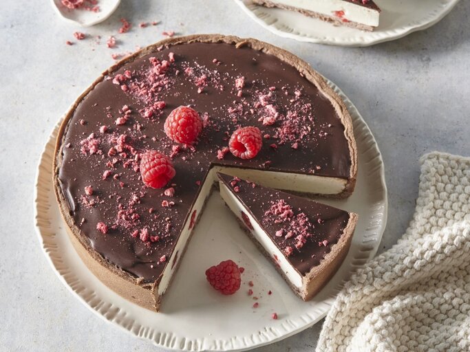 Auf einem Teller steht ein Käsekuchen mit Schokolade und Himbeeren. Er ist mit Himbeeren und Schokolade überzogen.  | © StockFood / Profimedia