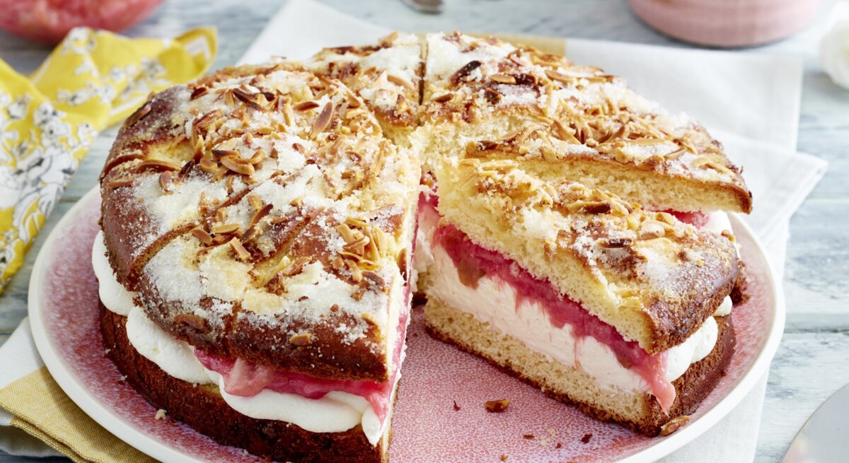 Auf einem Teller ist ein gefüllter Rhabarber-Butterkuchen angerichtet. Er ist mit Puderzucker bestreut.