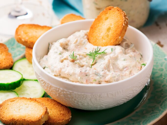 Lachscreme mit Frischkäse in weißer Schüssel mit Brotchips auf blauem Teller.  | © Getty Images/zoryanchik