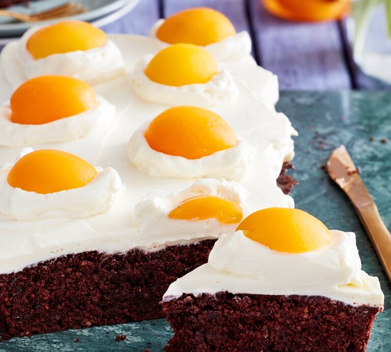 Auf einer Platte liegen Spiegeleier-Brownies. Sie sind mit Sprikosenhälften und einer Ricotta-Creme dekoriert und sehen aus wie aufgeschlagene Eier.  | © EAT CLUB/Isabell Triemer