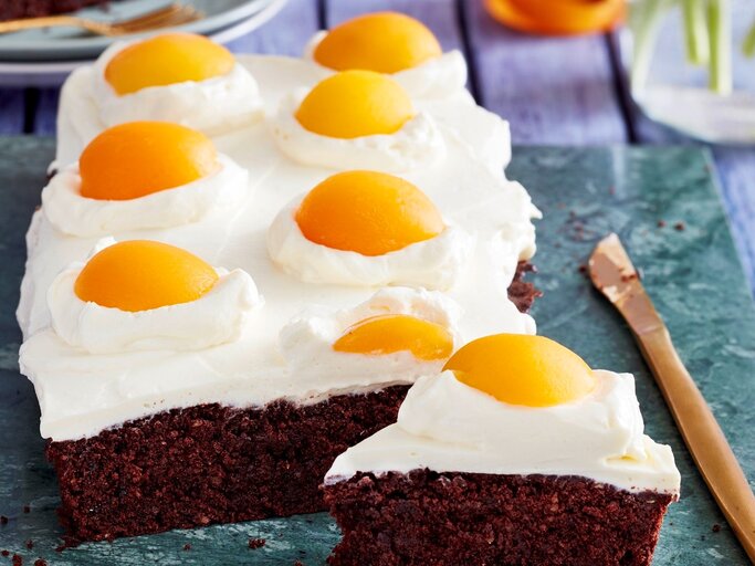 Auf einer Platte liegen Spiegeleier-Brownies. Sie sind mit Sprikosenhälften und einer Ricotta-Creme dekoriert und sehen aus wie aufgeschlagene Eier.  | © EAT CLUB/Isabell Triemer