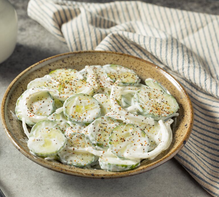 Sauerrahm-Gurkensalat mit frischem Pfeffer neben Geschirrtuch auf grauem Untergrund. | © Getty Images/bhofack2